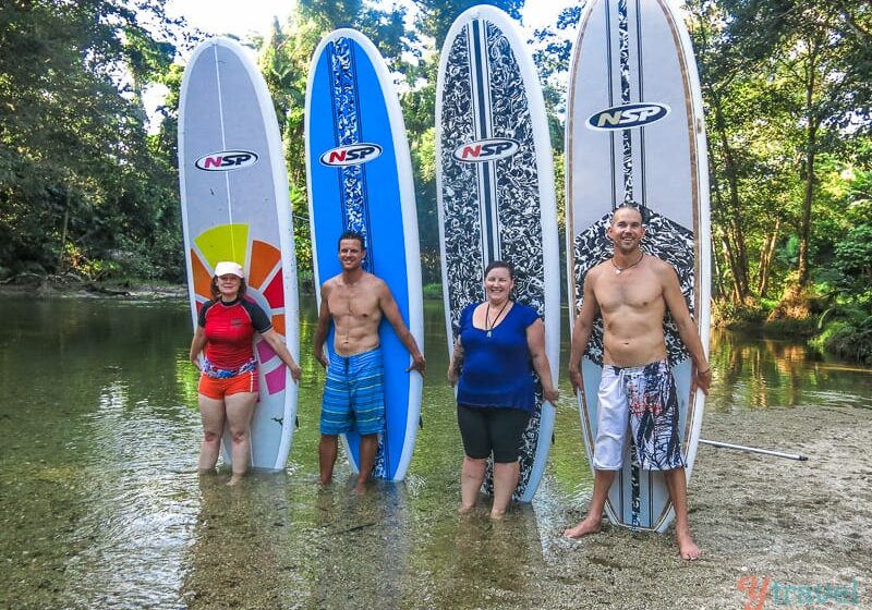 group of people standing in front of stand up paddle boards in a river